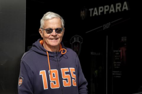 Jääkiekkovalmentaja Rauno Korpi hymyilee katsojalle. Hänellä on tummat silmälasit ja huppari.