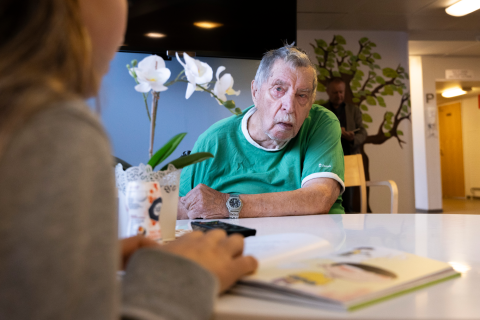 Henkilö istuu pöydän ääressä ja kuuntelee, kun hänelle luetaan.