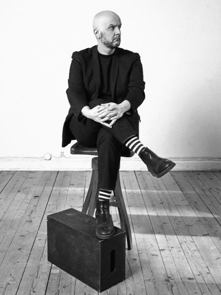 Jarno Alastalo istuu jakkaralla ja pitää jalkaa laatikon päällä. Taustalla valkoinen seinä. 